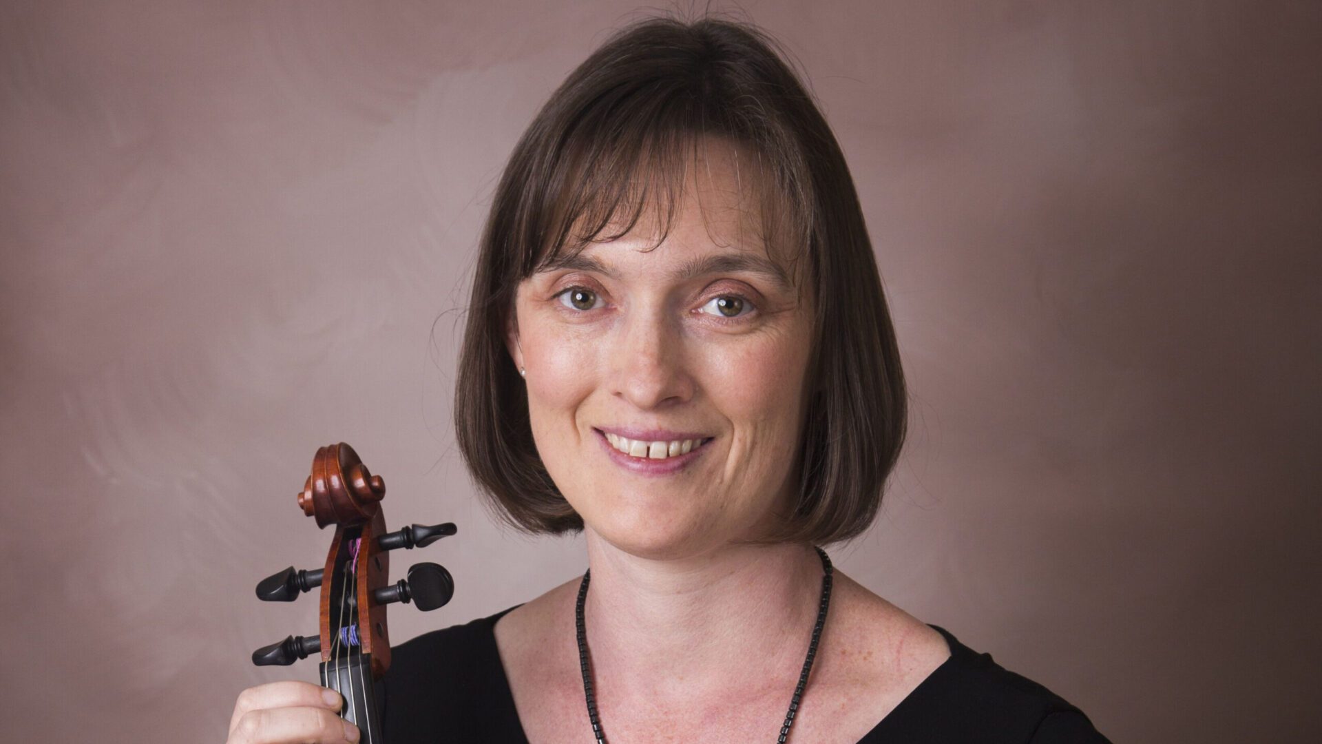 A woman holding a violin and smiling.