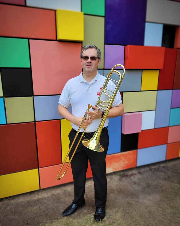 A man standing in front of a colorful wall with a trombone.