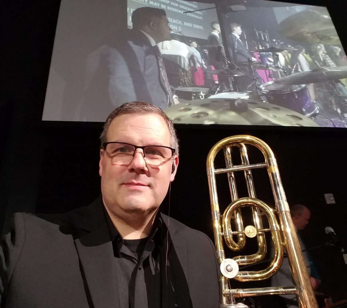 A man holding a trombone in front of a screen.