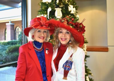 Two women in red hats standing in front of a christmas tree.