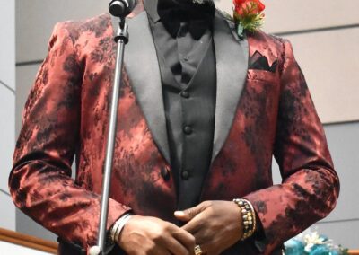 A man in a red tuxedo smiles into a microphone.