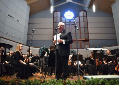 A man in a suit standing in front of an orchestra.